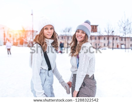 Two girls girlfriends winter in the city in the fresh air. Posing for the camera. In warm sweaters and hats. Happy smiling. Rest in the city on the rink.