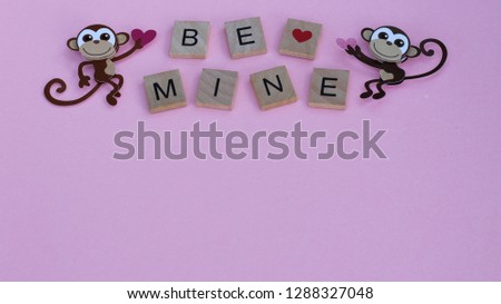 two monkeys holding valentine hearts next to the words be mine on wood tiles laying flat on a pink background with writing space