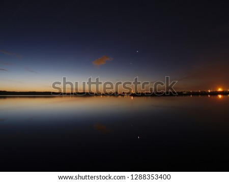 Twilight reflecting on lake surface, giving a beautiful colour pallet with a oil refinery at the right side. Birds traveling to the north for colder climate. With planets reflecting on lake surface.
