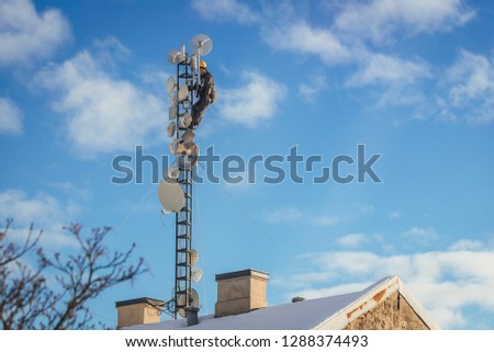 Telecom worker repairing antenna tower on blue sky background, cellular tower system.
