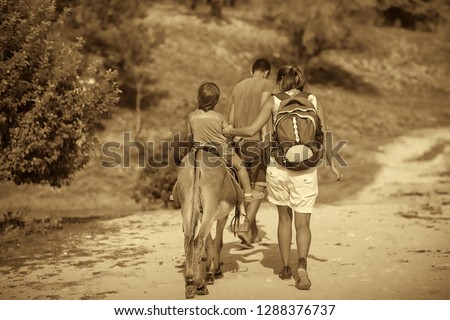 Summer, sunny day. Mom rolls the baby on a donkey on the road among the mountains of Crimea. Picture taken in Ukraine. Kiev region. Horizontal frame. Black and white image. Sepia toning
