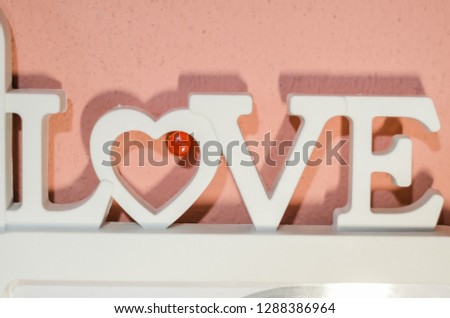 White word “Love” on the pink wall background. Place for writing something you need. Symbol of love. Happy Valentine’s day. White love frame for picture.