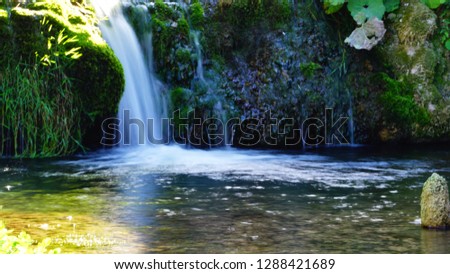 long exposure of small waterfalls of a stream between plants in a natural park on a sunny day