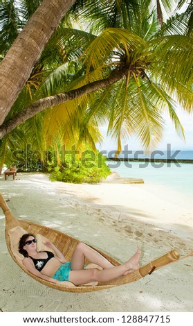 Girl is sleeping in the hammock under the palms on the tropical Maldivian beach