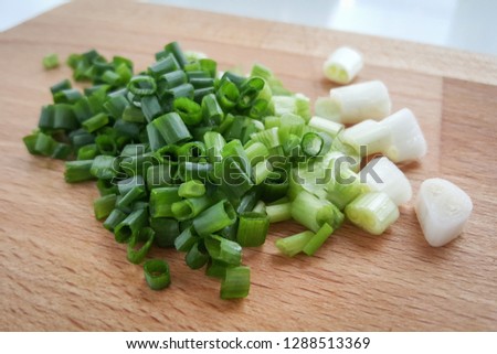Chopped scallion, onion leaf on wooden chopping board being prepared for cooking an asian dish. - close up