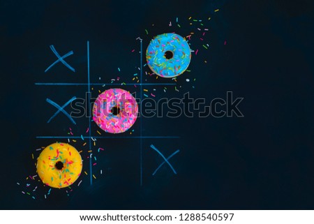 Glazed donuts tic-tac-toe game. Chalk drawing on a dark background with copy space. Creative food flat lay.