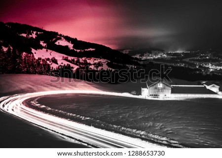 Long exposed night photography of cars driving through a snowy mountain road in the alps of Austria. Beautiful european winter night scene in Vorarlberg Austria.