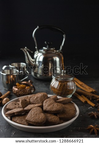 Vegan heart gingerbread cookies on dark background with cinnamon and anis stars. Metal kettke and cups. Tea christmas mood time.  Dark food photo