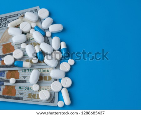 Pills on dollar money on blue background. Medicine expenses. High costs of medication concept. Close up.