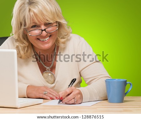 Happy Mature Woman Writing On Paper against a green background