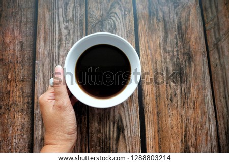 Woman hand holding a cup of coffee on wooden table.