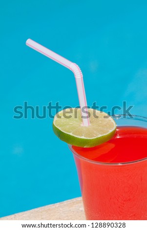 Red Beverage in plastic cup with Straw and Lime beside the pool