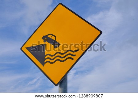 Sign Caution Car falling from Pier.  Diamond shape, yellow background on an angle against blue sky and clouds