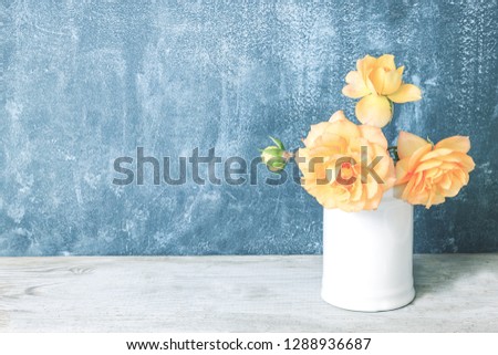 Yellow roses in retro white vase on wood table on blue wall with copy space. Beautiful bouquet of roses