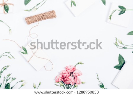 Feminine festive flat layout with pink bouquet, eco gift boxes, leaves, green stems and jute rope, top view. Stylish celebration decor frame on white background with empty place in center.