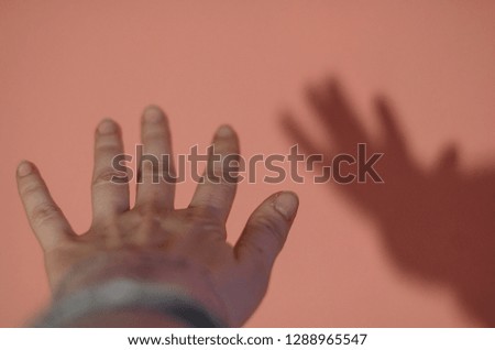 A hand of a human is trying to reach something. Pink wall background. The shadow game concept