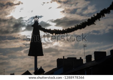 silhouette of Christmas tree with sun directly behind and rooftops in the background