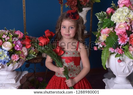 portrait of a little princess girl in a red dress with flowers in her hands and around her