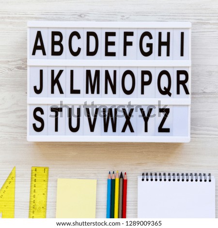 Education concept. Letters from A to Z. English alphabet on lightbox and accessories for study over white wooden desk, overhead view. From above, flat lay, top view.