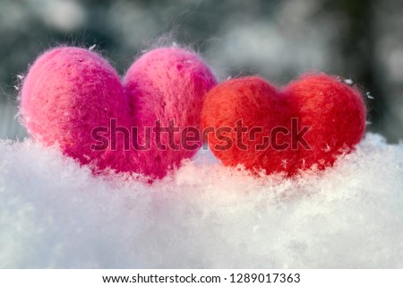 Two wool red and pink hearts standing on the white fluffy snow in winter. Symbols of love. Love, healtcare, valentines day concept.                            