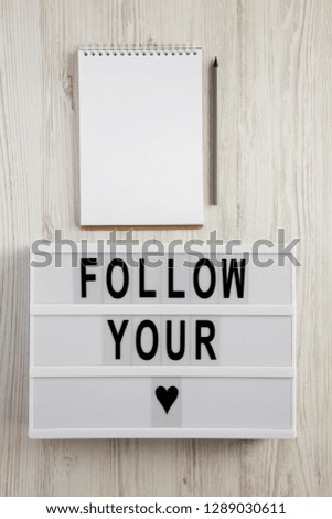 Modern board with text 'Follow you heart', blank notepad over white wooden background. Valentine Day 14 February.