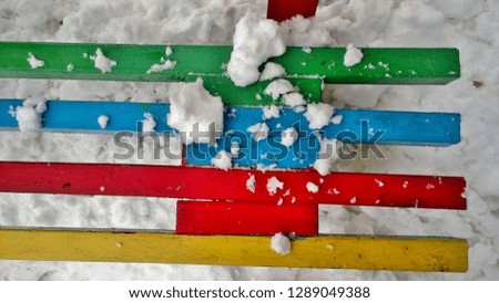Texture, background, wallpaper of a multi-colored bench with white snow in the afternoon in the winter.