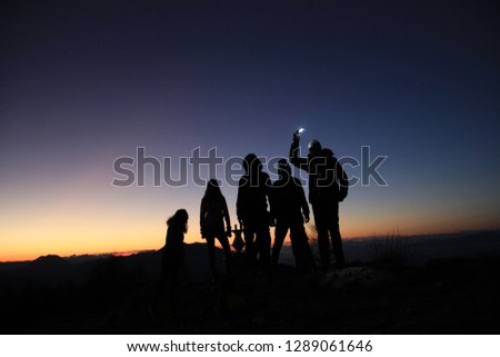 Fife young pepople standing on the top mountain on the sunset. One boy keeps the light.Dark blue and orange sky. 