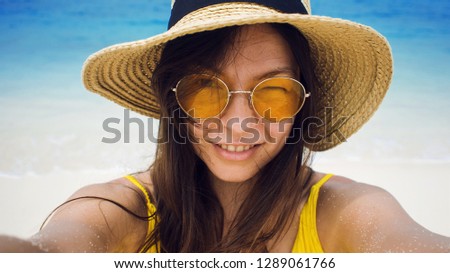 Happy girl on vacation. Young brunette in a straw hat and sunglasses, taking a selfie against the sea.