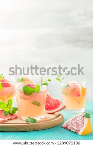 Fresh pink alcoholic cocktail with grapefruit, ice and mint, drink glasses and ingredients on a blue turquoise table, selective focus, shallow depth of the field.