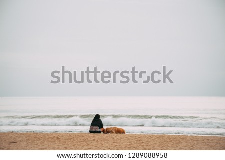 Lonely girl and dog sitting on the tropical beach looking out to sea and sky. Concept of holiday, summer vacation, relaxation and beautiful friendship. Copy space.