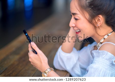 portrait asian girl wearing white shirt in outdoor with smile relaxing sit on the chair in coffee outdoor by looking phone