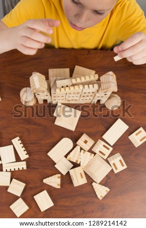 Boy building a castle using wooden blocks on a desk at home, learning final motor skills. Focus on the castle. 
