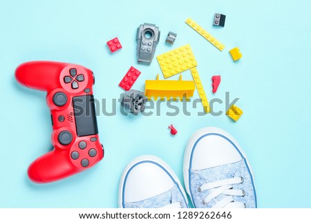 Shoes and children's 80s entertainment and toys on a blue background. Red gamepad, children's constructor bricks, sneakers, top view
