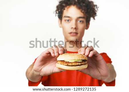 Curly guy in a red shirt holds a fast food hamburger         