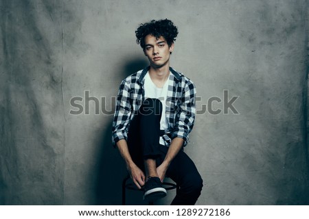 Curly guy in shirt and t-shirt sneakers black pants on a high chair               