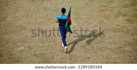 Young boy running with a Bangladeshi national flag around a field