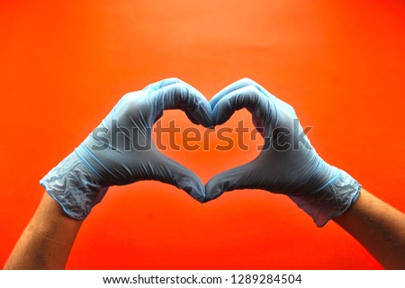 Hands in medical latex gloves. Hands form a heart shape. The gesture symbolizes the declaration of love. Red background. Close-up. Concept: Hand gestures for expressing emotions.