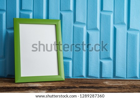 Green photo frame on old wooden table over blue wallpaper background