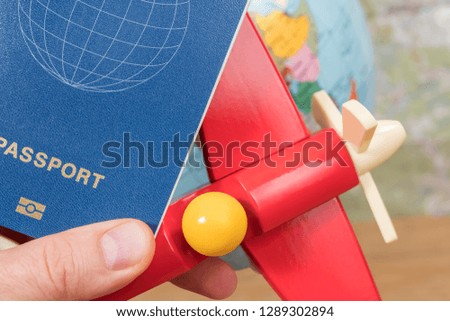 Passport and toy airplane in male hand on the background of the globe on the table