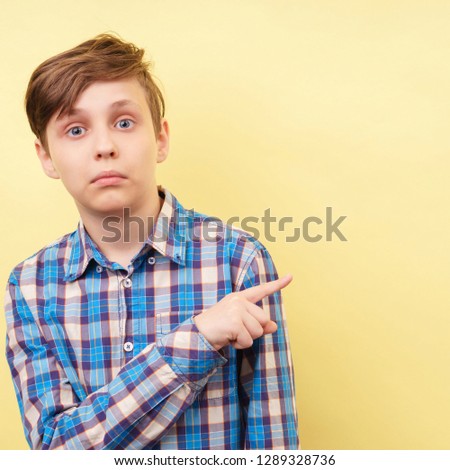 surprised startled amazed astounded and stunned boy points with index finger at empty space over yellow background, advertisement, banner or poster template, emotion facial expression, people reaction