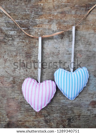 Two fabric or textile stripped pastel pink and blue harts hanging from a rope against rustic wooden background. Love, couple or Valentine's day background