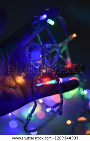 Male hand with garland LED light as Christmas holiday decoration on bokeh background