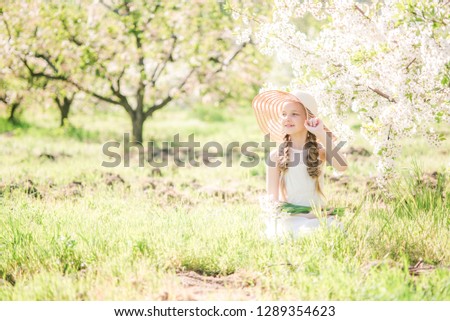 Cute girl with blond hair in a white sundress in spring in a lush garden with daffodils
