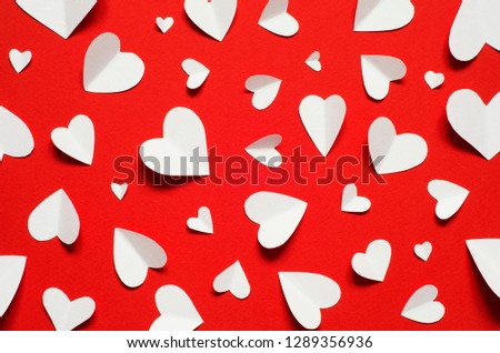Valentine's day romantic background. White paper hearts at red backdrop, top view.