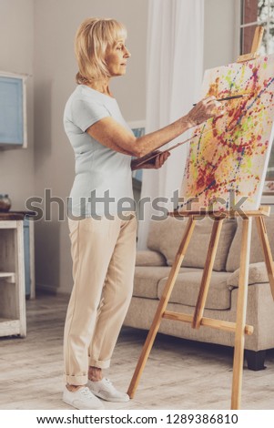 More colors. Serious woman standing in semi position while enjoying the process of art