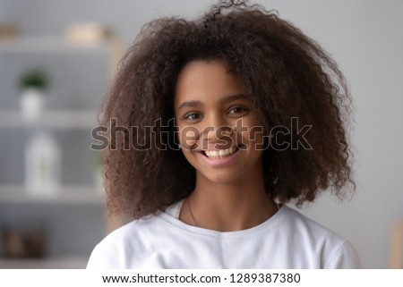 Portrait of happy African American teen girl looking at camera at home, headshot of smiling black teenager posing indoors, beautiful mixed race teenage female laughing making picture