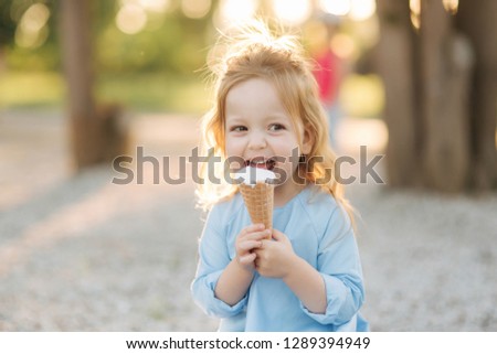 Beautiful little girl in a blue dress eating an ice cream Royalty-Free Stock Photo #1289394949
