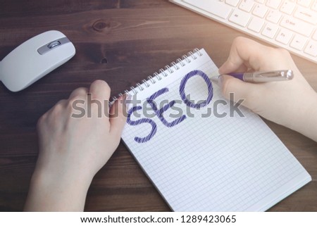 Woman doing SEO writing in a notebook that lies on a wooden, old Desk