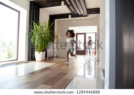 Happy little black girl running exploring big luxury house moving in, parents and excited kid daughter entering new home, cute mixed race child having fun jump in hallway, african family mortgage Royalty-Free Stock Photo #1289446888