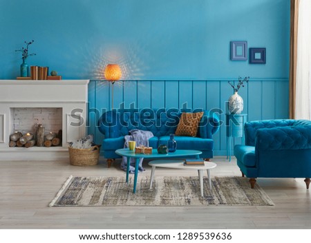 Blue room decoration, blue sofa and wall concept, white fireplace with wood, frame and middle table and carpet decoration. Lamp and frame style.